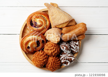 Assorted sweet pastries and baked goods on a wooden plate arranged for dessert enjoyment 121938098