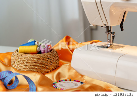 Sewing machine in use on a wooden table, stitching a light fabric in a well-lit indoor workspace 121938133