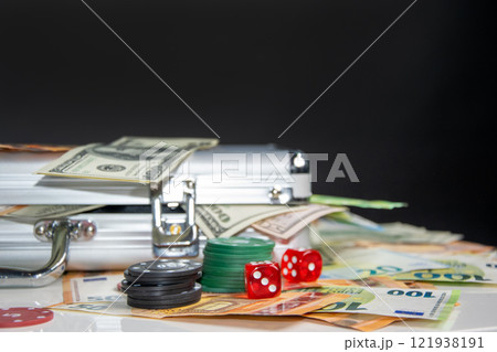A silver case containing stacks of cash with dice and poker chips on a table A silver case containing stacks of cash with dice and poker chips on a table 121938191