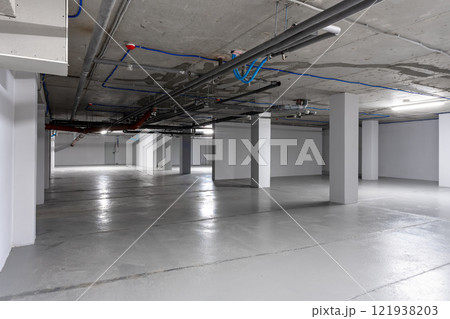 Empty underground parking garage with exposed pipes and clean concrete floors in a modern structure Empty underground parking garage with exposed pipes and clean concrete floors in a modern structure 121938203