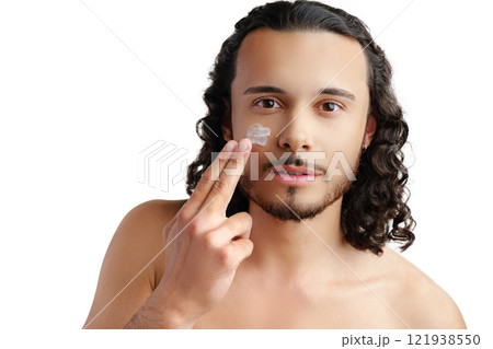A young man demonstrates skincare routine with moisturizer on his face 121938550