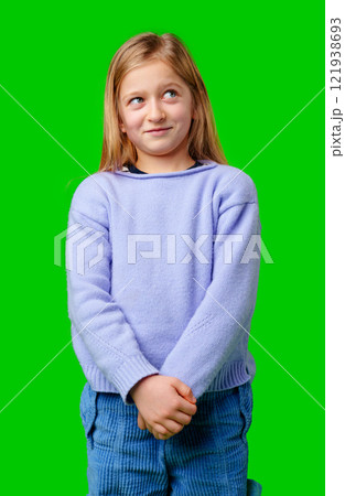 A young child in a light purple sweater gazes against a green background while deep in thought A young child in a light purple sweater gazes against a green background while deep in thought 121938693