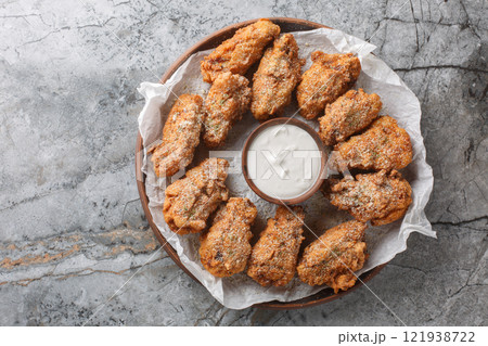 Breaded Bburinkle fried chicken wings in cheese garlic onion breading with dipping sauce close-up in plate. Horizontal top view 121938722