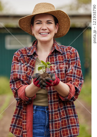 Sustainable farmer holding a plant or seedling outdoors smiling and happy about her organic farm or garden. Young female nature activist that is passionate about sustainability standing on farmland 121938790