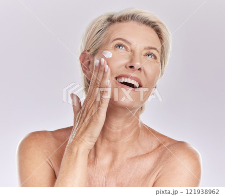 Woman with sunscreen on face for beauty skincare, showing cosmetics with smile and care for skin wellness standing on grey studio background. Content elderly model doing self care with cream 121938962