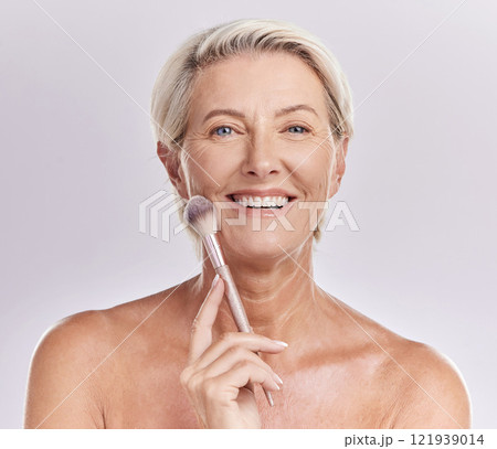 Beauty, skincare and makeup with a senior woman applying cosmetics to her face in studio against a purple background. Head portrait of a female with blusher looking beautiful, happy and healthy Beauty, skincare and makeup with a senior woman applying cosmetics to her face in studio against a purple background. Head portrait of a female with blusher looking beautiful, happy and healthy 121939014
