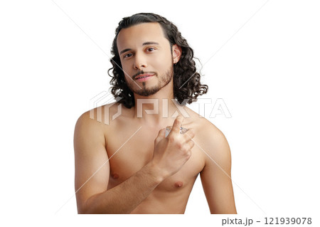 A young man with curly hair applying fragrance after a shower while smiling at the camera 121939078