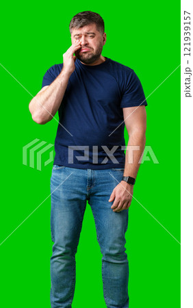 Man expressing frustration with tired eyes while standing in front of a bright green background 121939157