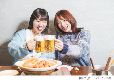 カニ鍋を前に乾杯をする若い女性二人【撮影協力・海鮮居酒屋 魚魯こ】 カニ鍋を前に乾杯をする若い女性二人【撮影協力・海鮮居酒屋 魚魯こ】 121939206