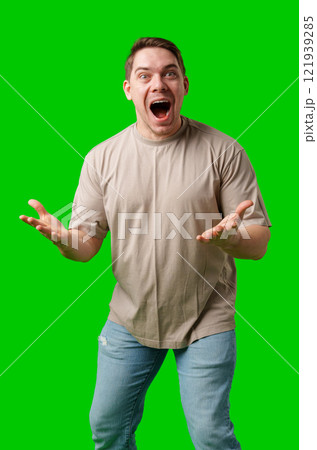 Young man in casual clothing stands with open arms against a vibrant green background 121939285