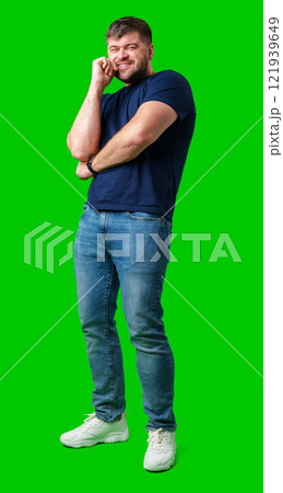 A man in a blue shirt and jeans poses confidently with a friendly smile against a bright green backdrop 121939649