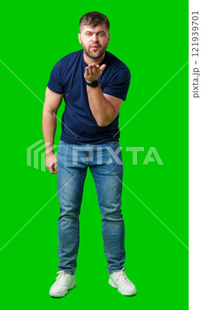 A man blowing a kiss while standing against a bright green backdrop in a casual outfit A man blowing a kiss while standing against a bright green backdrop in a casual outfit 121939701