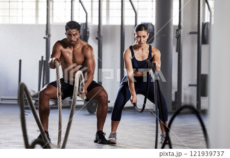 Active, fitness partners training together, exercising with battle ropes in gym. Athletic sports couple in motion doing arms and cardio workout in wellness center for strength and healthy lifestyle. Active, fitness partners training together, exercising with battle ropes in gym. Athletic sports couple in motion doing arms and cardio workout in wellness center for strength and healthy lifestyle. 121939737
