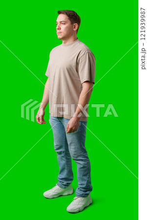A young man stands confidently in casual attire on a vibrant green background A young man stands confidently in casual attire on a vibrant green background 121939987