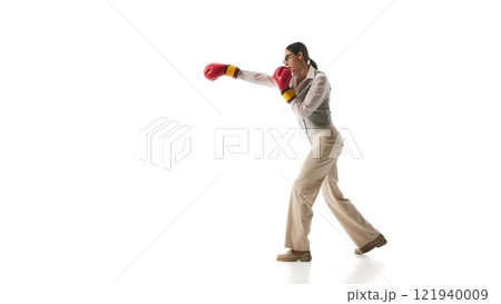 Focused woman in gray vest and beige trousers steps into precise boxing stance, symbolizing determination and adaptability against white studio background. Focused woman in gray vest and beige trousers steps into precise boxing stance, symbolizing determination and adaptability against white studio background. 121940009