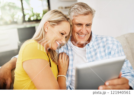 Happy, relaxed and in love mature couple watching a movie together on a tablet online while relaxing on a couch indoors at home. Smiling senior man and woman streaming their entertainment tv series 121940561