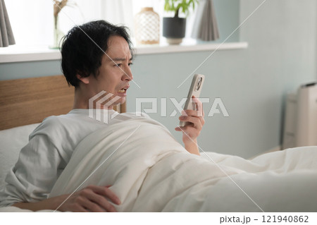 ベッドでスマホを見る男性 121940862