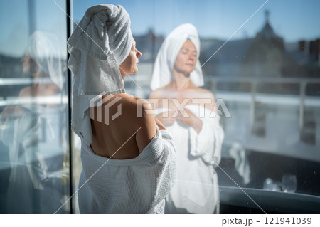 Back view of young woman with towel on her head looking out the window Back view of young woman with towel on her head looking out the window 121941039