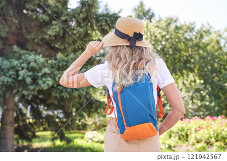 Young caucasian female backpacker in straw hat exploring scenic summer park 121942567