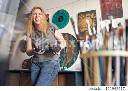 Caucasian female artist showcasing art in studio with paintings and brushes Caucasian female artist showcasing art in studio with paintings and brushes 121942617