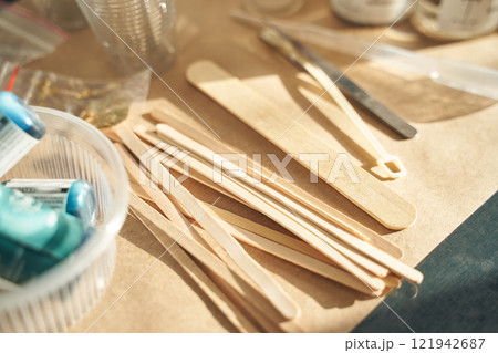 Wooden craft sticks and tools arranged on a workshop table with blue glue tubes Wooden craft sticks and tools arranged on a workshop table with blue glue tubes 121942687