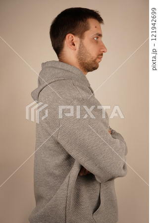 Side view. Handsome guy. Neutral background. Man in casual clothes. Young man standing in front of camera. Male looking at side. Crossed hands. 121942699