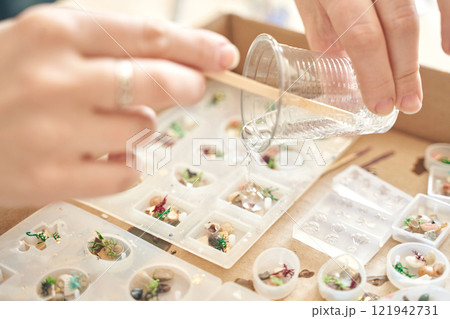 Hands pouring resin into molds for artistic jewelry making at craft workshop 121942731