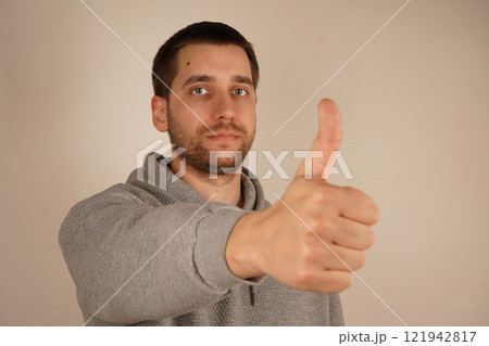Okay sign. Agree. Charming confident guy dressed gray hoodie showing thumb up alone. Young handsome man with beard over isolated gray background giving a thumbs up gesture. 121942817
