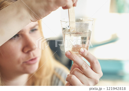 Caucasian young female examining clear liquid in a glass cup with wooden 121942818