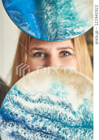 Caucasian female artist with blue resin art disks displaying ocean inspired 121942822