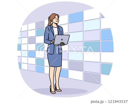 Woman working at telecommunications company stands near wall of displays and holds laptop in hands Woman working at telecommunications company stands near wall of displays and holds laptop in hands 121943537