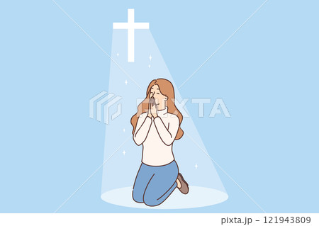 Christian woman prays on knees under religious crucifix or cross emitting bright light Christian woman prays on knees under religious crucifix or cross emitting bright light 121943809