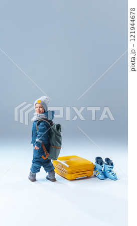 Little tourist, pre-school boy dressed winter clothes standing with backpack near huge suitcase, ready to adventures, against grey background. Little tourist, pre-school boy dressed winter clothes standing with backpack near huge suitcase, ready to adventures, against grey background. 121944678