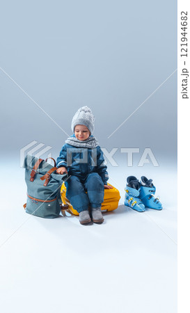 Little explorer, curious little kid, dressed warm clothes, sitting on yellow suitcase, ready to adventures, against grey studio background. 121944682