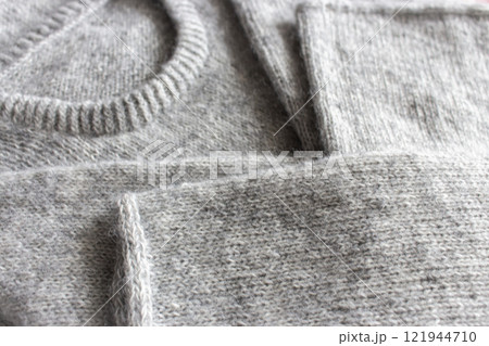 Grey melange knitting sweater with i-cord bind off. Mix of grey wool and white cashmere. Knitting pattern background. Knitting lifestyle. Cozy hobby. Warm knitwear. Craft product concept. Grey melange knitting sweater with i-cord bind off. Mix of grey wool and white cashmere. Knitting pattern background. Knitting lifestyle. Cozy hobby. Warm knitwear. Craft product concept. 121944710