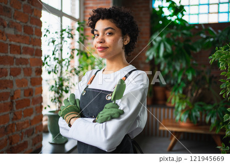 Running of own business. African woman florist wearing apron in botanical store with green plants. Happy small business owner working at flower shop smiling surrounded by plants Small business 121945669