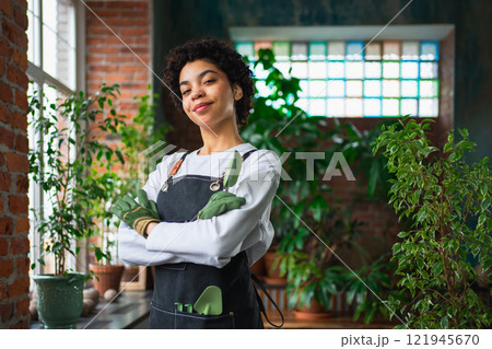 Running of own business. African woman florist wearing apron in botanical store with green plants. Happy small business owner working at flower shop smiling surrounded by plants Small business 121945670
