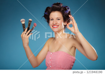 woman in hair rollers holds makeup brushes 121948190