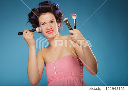 woman in hair rollers holds makeup brushes 121948191
