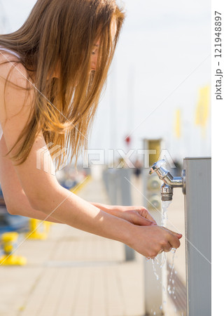 Woman drinking water from tap in marina. 121948897