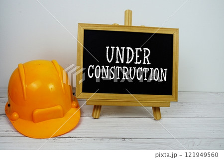Under Construction text on blackboard with safety helmet on wooden background Under Construction text on blackboard with safety helmet on wooden background 121949560