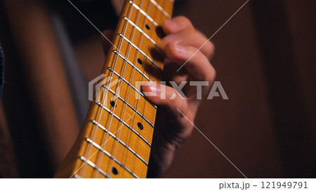 Detailed view of a vintage-style maple fretboard with position dots and nickel frets. The warm amber finish and blurred hand positioning create a nostalgic mood against a dark background Detailed view of a vintage-style maple fretboard with position dots and nickel frets. The warm amber finish and blurred hand positioning create a nostalgic mood against a dark background 121949791