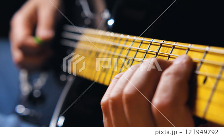 Close-up of hands playing an electric guitar with a distinctive yellow fretboard. The shallow depth of field creates a moody atmosphere while highlighting the metallic frets and strings Close-up of hands playing an electric guitar with a distinctive yellow fretboard. The shallow depth of field creates a moody atmosphere while highlighting the metallic frets and strings 121949792