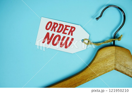 Order Now on price tag with wooden clothes hanger top view on blue background, business and promotion concep Order Now on price tag with wooden clothes hanger top view on blue background, business and promotion concep 121950210
