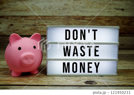 Don't waste money text on LED lightbox with piggy saving on wooden background, Money concept Don't waste money text on LED lightbox with piggy saving on wooden background, Money concept 121950231