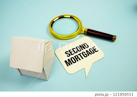 Second Mortgage text message on sticky note with magnifying glass and house model on blue background 121950551