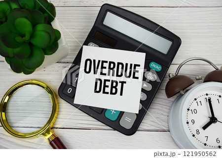Overdue Debt text message on sticky note with magnifying glass, alarm clock and calculator on wooden background 121950562