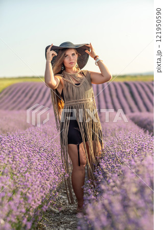 A woman is standing in a field of purple flowers, wearing a black dress and a black hat. A woman is standing in a field of purple flowers, wearing a black dress and a black hat. 121950590