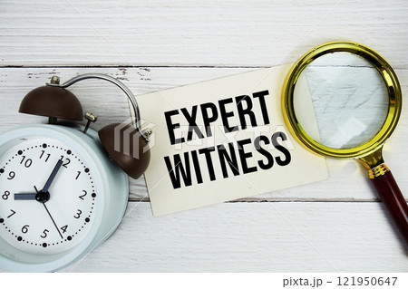 Expert Witness text message on sticky note with magnifying glass and alarm clock on wooden 121950647