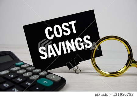 Cost Savings text message on sticky note with magnifying glass and calculator on wooden 121950782
